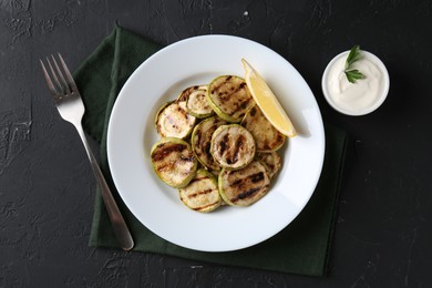 Tasty grilled zucchini slices served on black textured table, flat lay