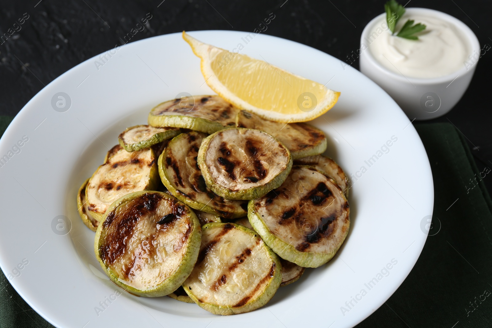 Photo of Tasty grilled zucchini slices served on black table