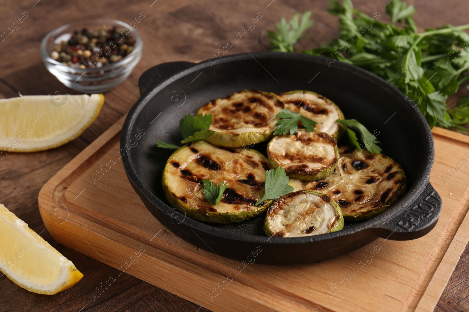 Photo of Tasty grilled zucchini slices with parsley in dish served on wooden table