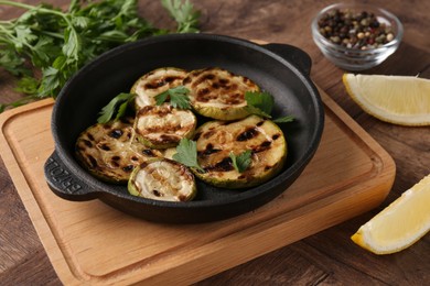 Photo of Tasty grilled zucchini slices with parsley in dish served on wooden table