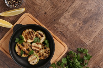 Tasty grilled zucchini slices with parsley in dish served on wooden table, flat lay. Space for text