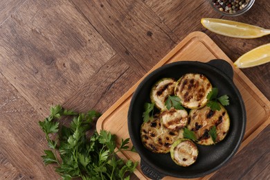 Photo of Tasty grilled zucchini slices with parsley in dish served on wooden table, flat lay. Space for text