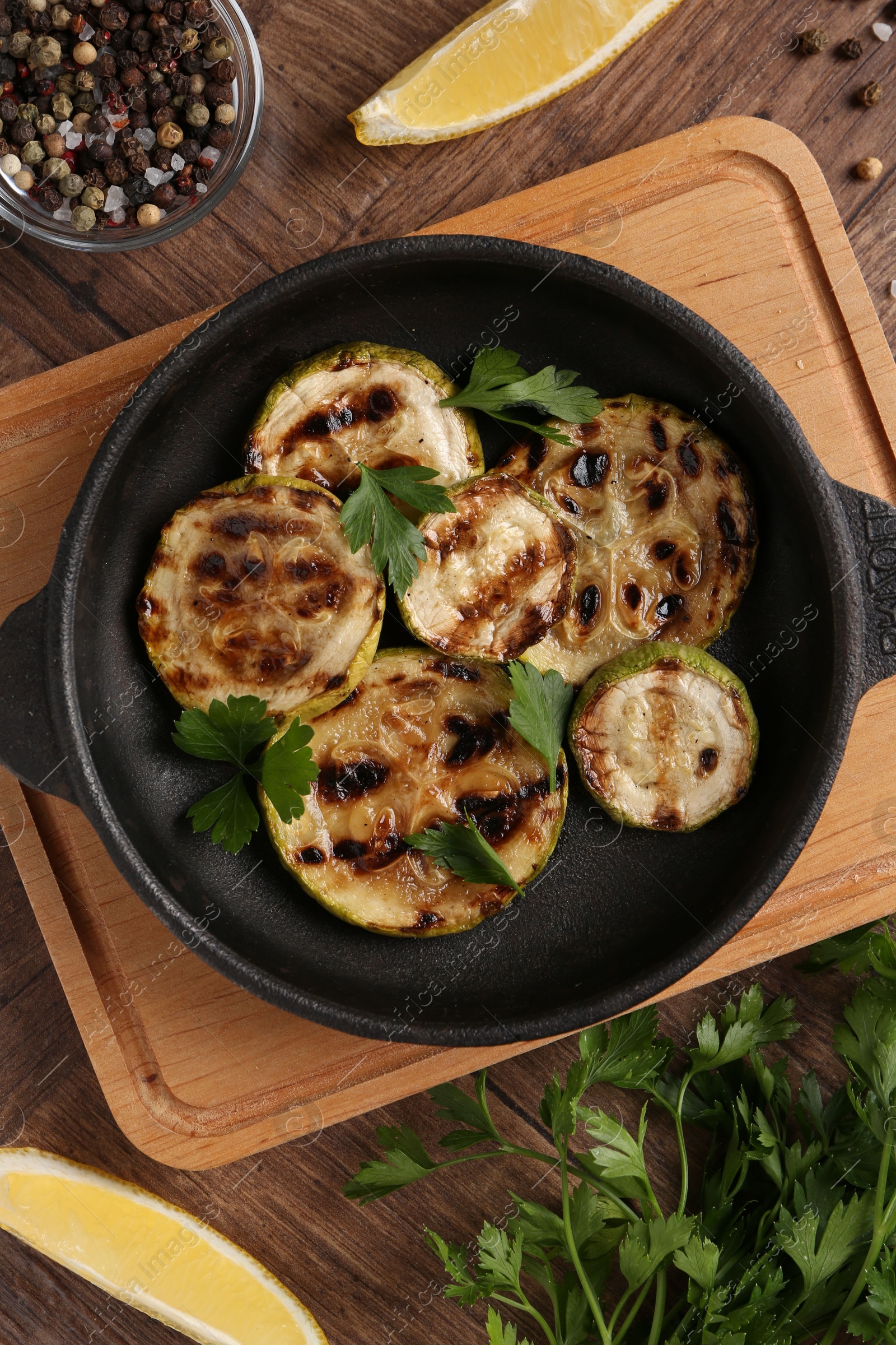 Photo of Tasty grilled zucchini slices with parsley in dish served on wooden table, flat lay