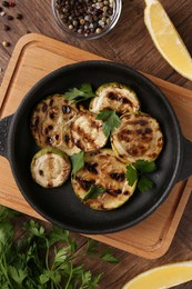 Photo of Tasty grilled zucchini slices with parsley in dish served on wooden table, flat lay