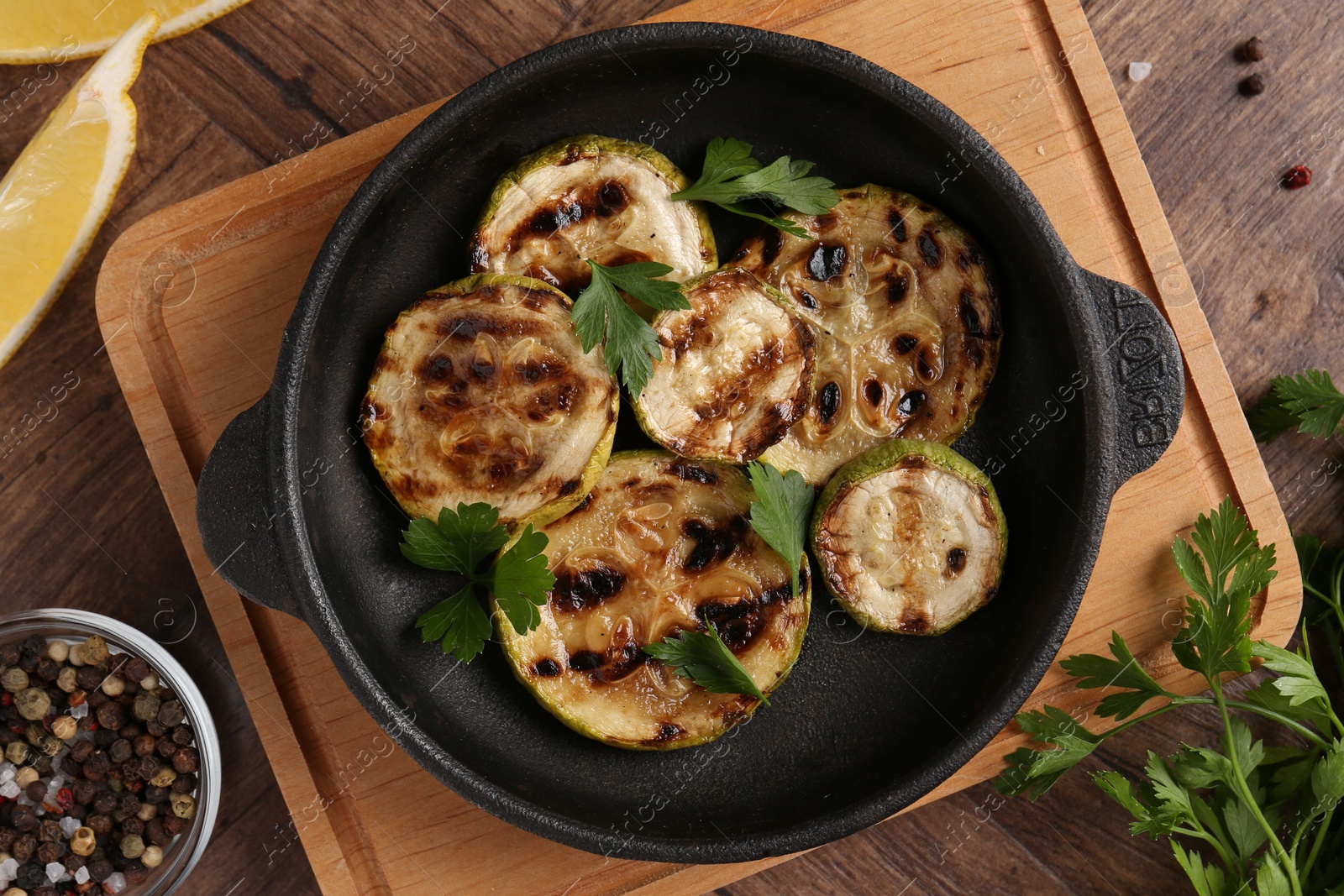 Photo of Tasty grilled zucchini slices with parsley in dish served on wooden table, flat lay