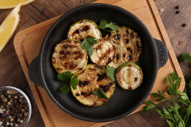 Tasty grilled zucchini slices with parsley in dish served on wooden table, flat lay