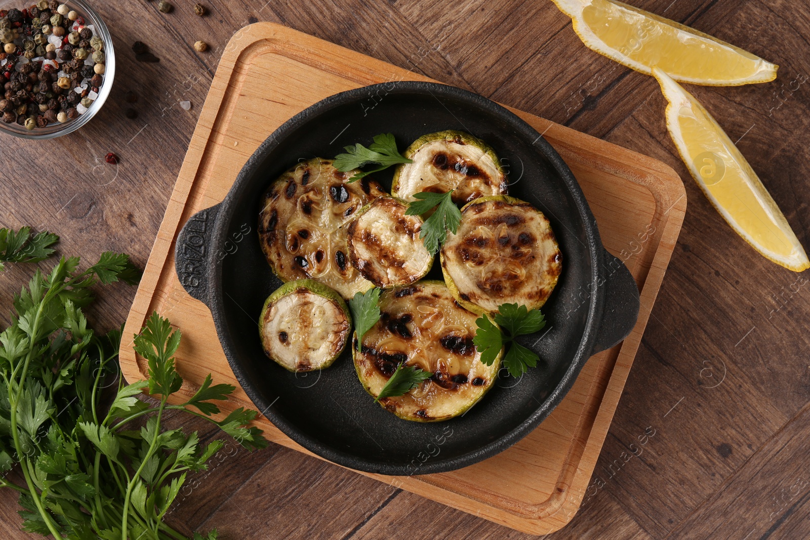 Photo of Tasty grilled zucchini slices with parsley in dish served on wooden table, flat lay