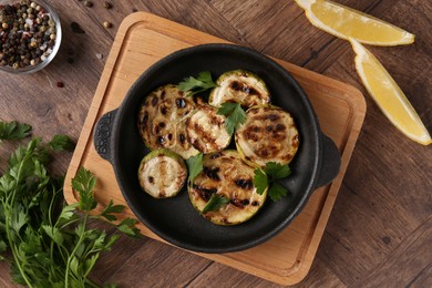 Tasty grilled zucchini slices with parsley in dish served on wooden table, flat lay