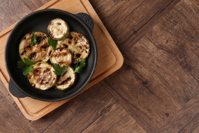 Photo of Tasty grilled zucchini slices with parsley in dish on wooden table, top view. Space for text