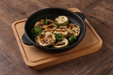 Photo of Tasty grilled zucchini slices with parsley in dish on wooden table