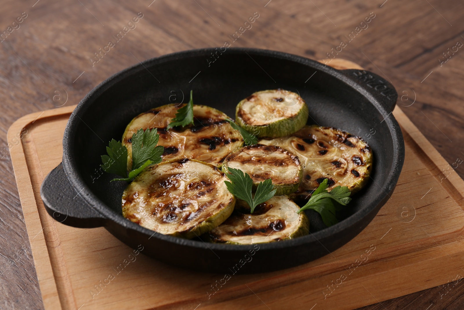 Photo of Tasty grilled zucchini slices with parsley in dish on wooden table