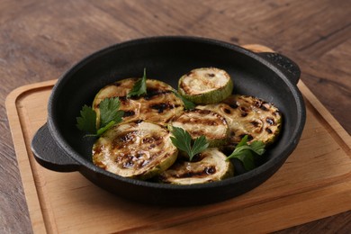 Tasty grilled zucchini slices with parsley in dish on wooden table