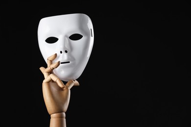 Photo of Wooden mannequin hand holding plastic mask on black background, space for text. Theatrical performance