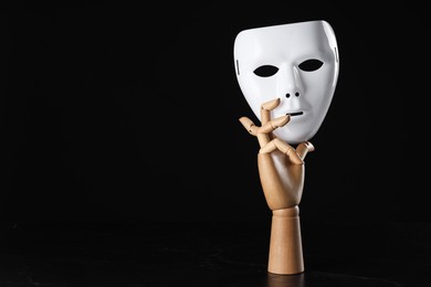 Wooden mannequin hand holding plastic mask on black background, space for text. Theatrical performance