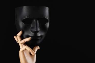 Wooden mannequin hand holding plastic mask on black background, space for text. Theatrical performance