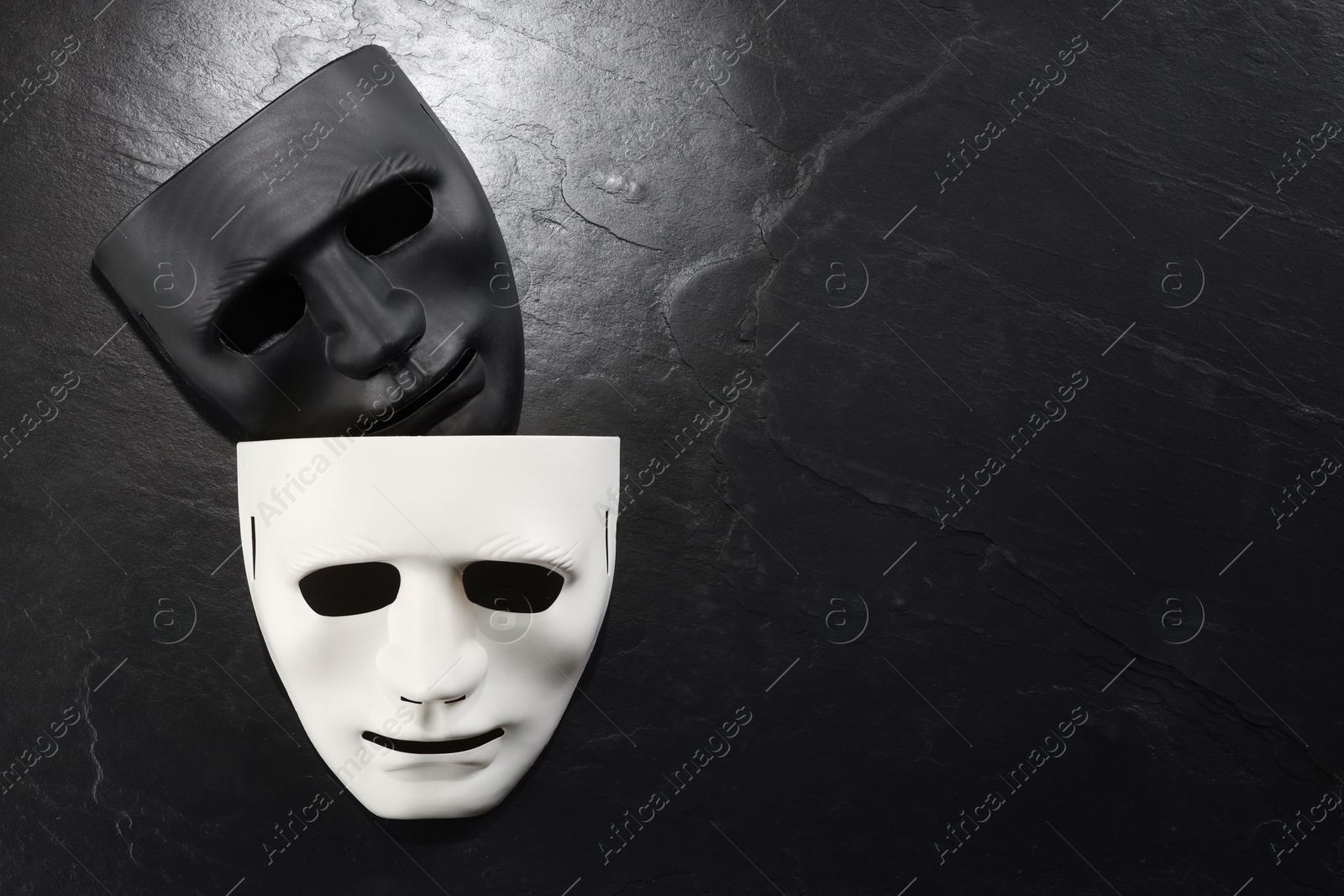 Photo of Plastic face masks on black slate surface, top view and space for text. Theatrical performance