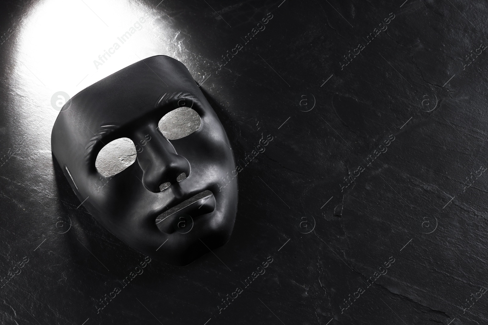 Photo of Plastic face mask on black slate surface, top view and space for text. Theatrical performance