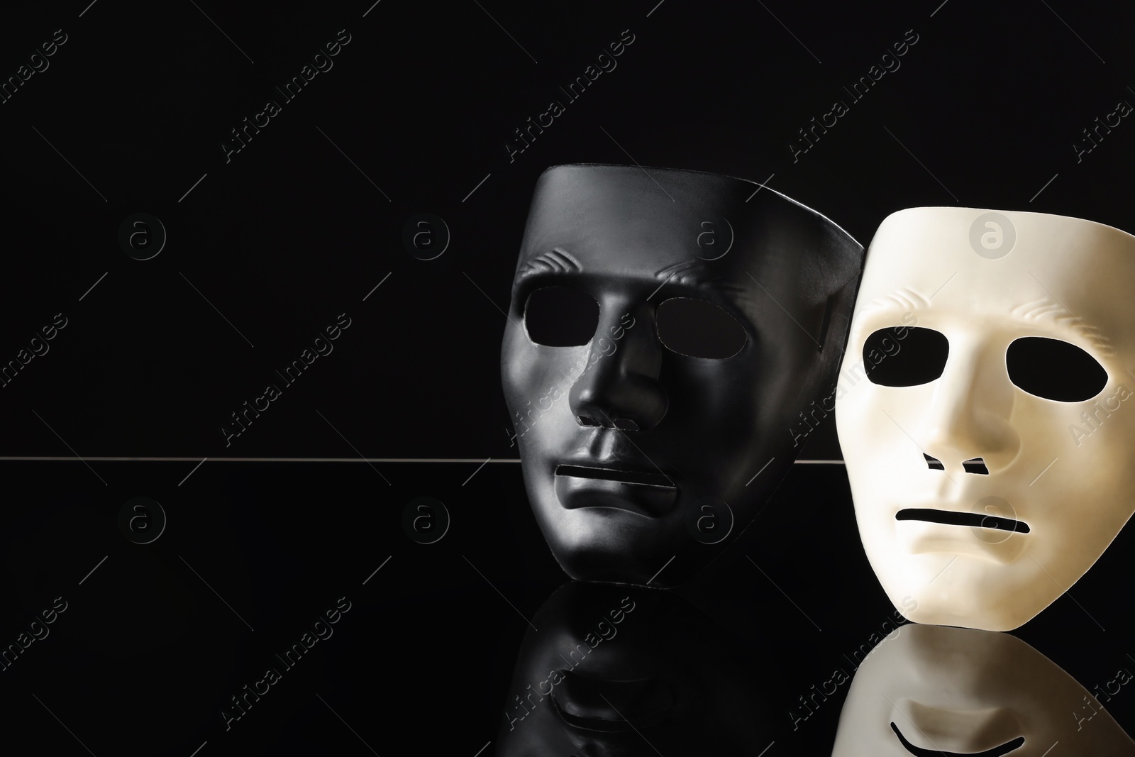 Photo of Plastic face masks on black mirror surface, space for text. Theatrical performance