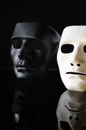 Photo of Plastic face masks on black mirror surface. Theatrical performance