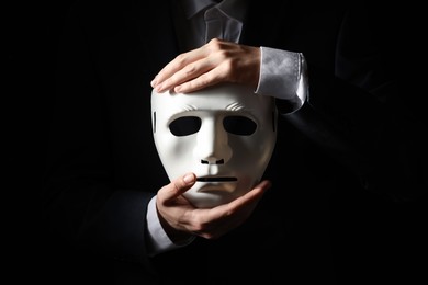 Theatrical performance. Man holding plastic mask on black background, closeup