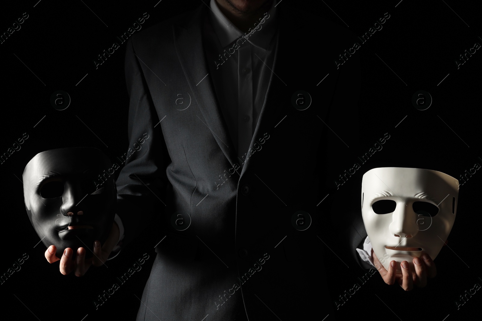 Photo of Theatrical performance. Man holding plastic masks on black background, closeup