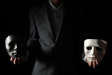 Photo of Theatrical performance. Man holding plastic masks on black background, closeup