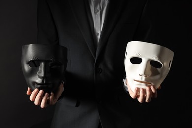 Photo of Theatrical performance. Man holding plastic masks on black background, closeup