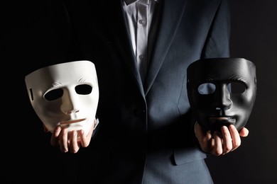 Photo of Theatrical performance. Man holding plastic masks on black background, closeup