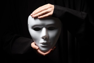 Theatrical performance. Man holding plastic mask on black background, closeup