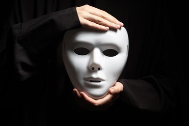 Photo of Theatrical performance. Man holding plastic mask on black background, closeup