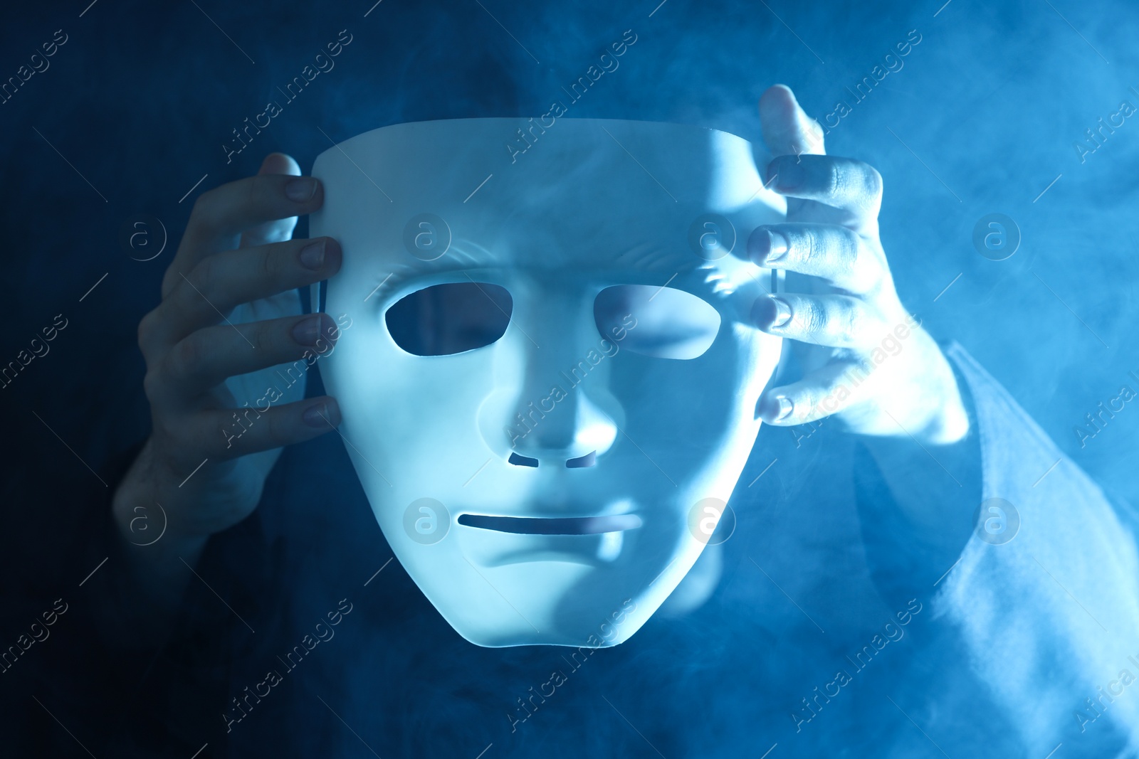 Photo of Theatrical performance. Man with plastic mask in smoke on dark background, closeup