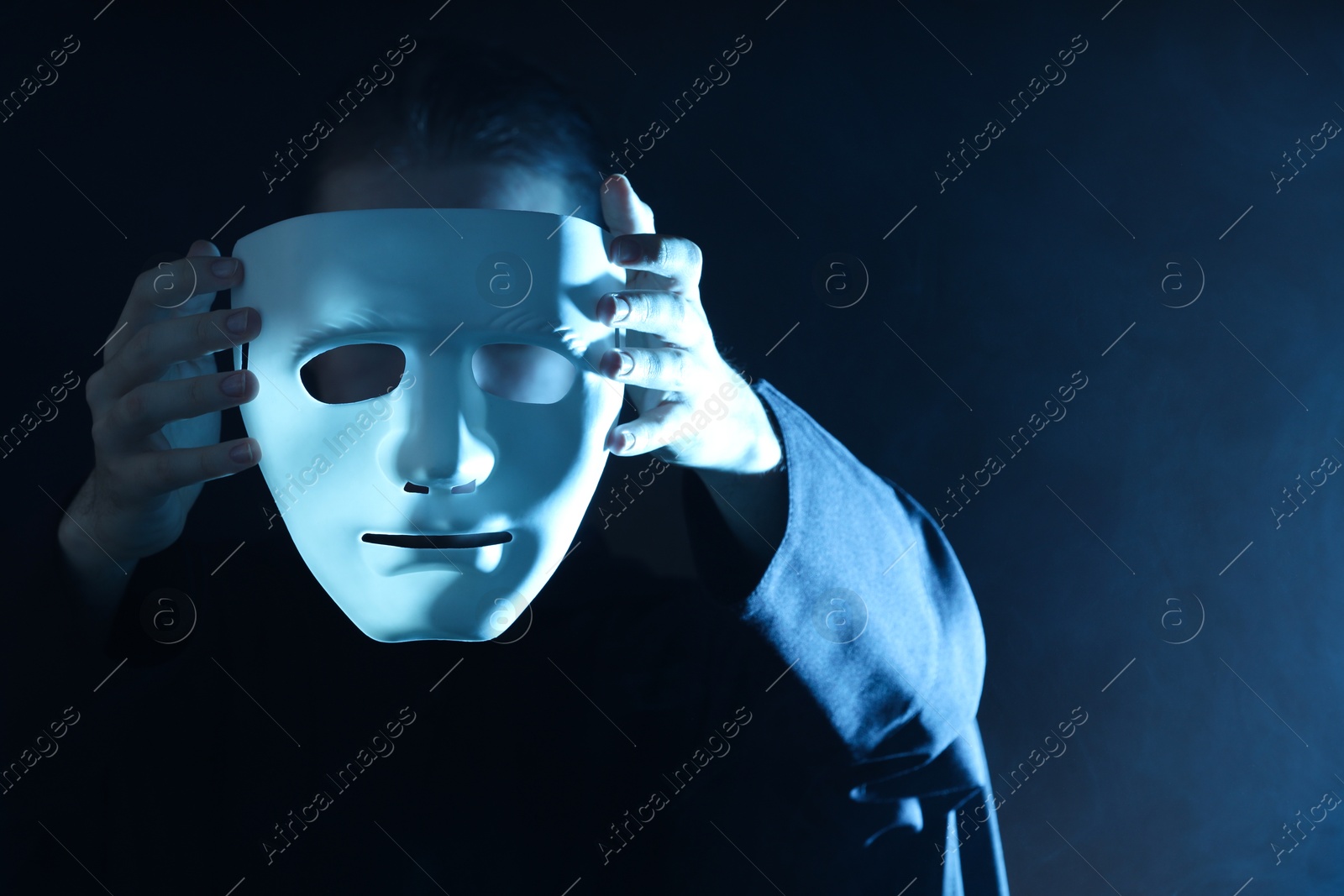 Photo of Theatrical performance. Man with plastic mask in smoke on dark background, closeup