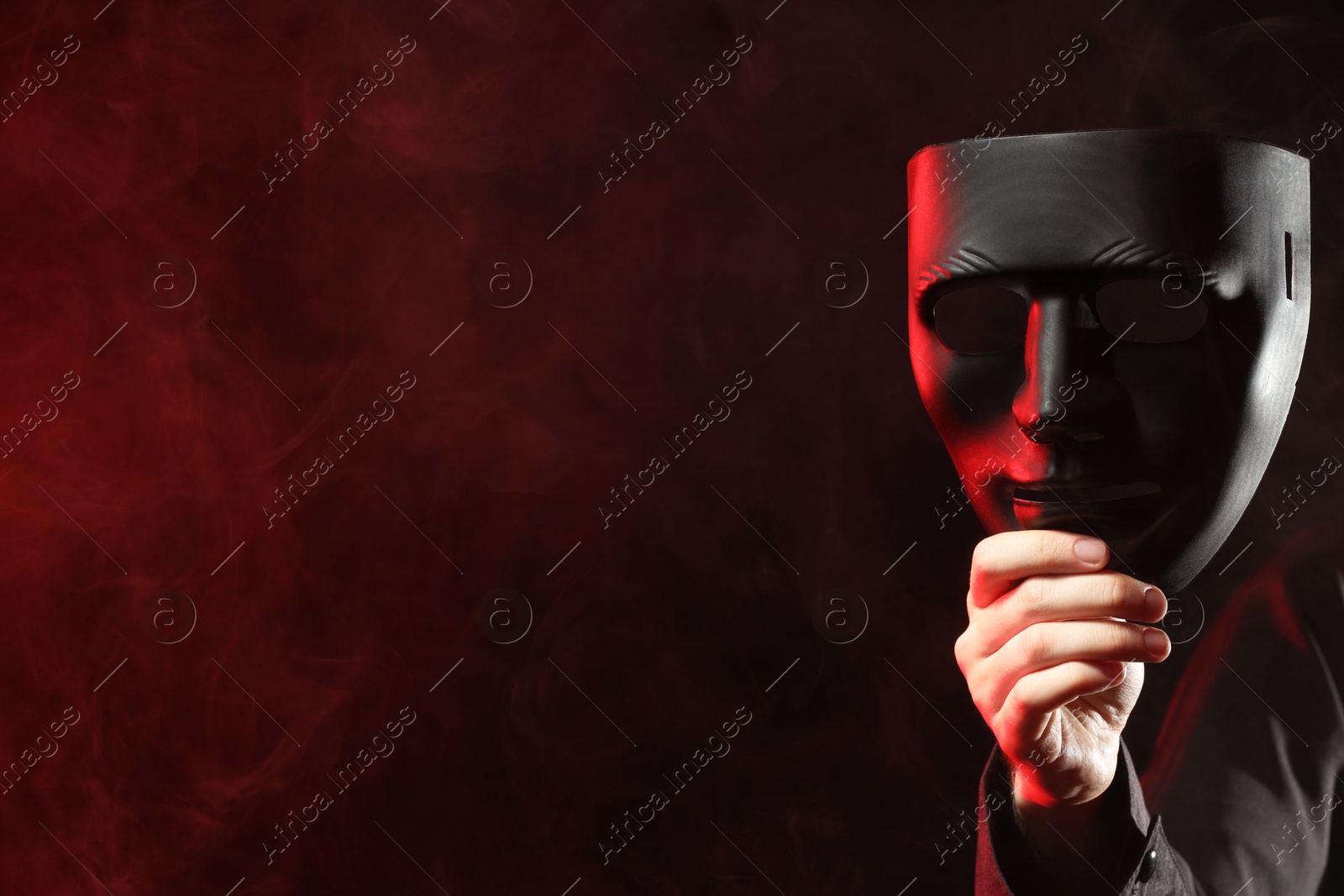 Photo of Theatrical performance. Man with plastic mask in smoke on dark background, closeup. Space for text