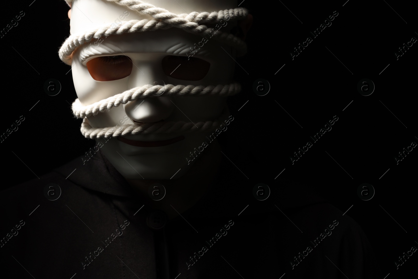 Photo of Theatrical performance. Man with plastic mask and hemp rope on black background, space for text