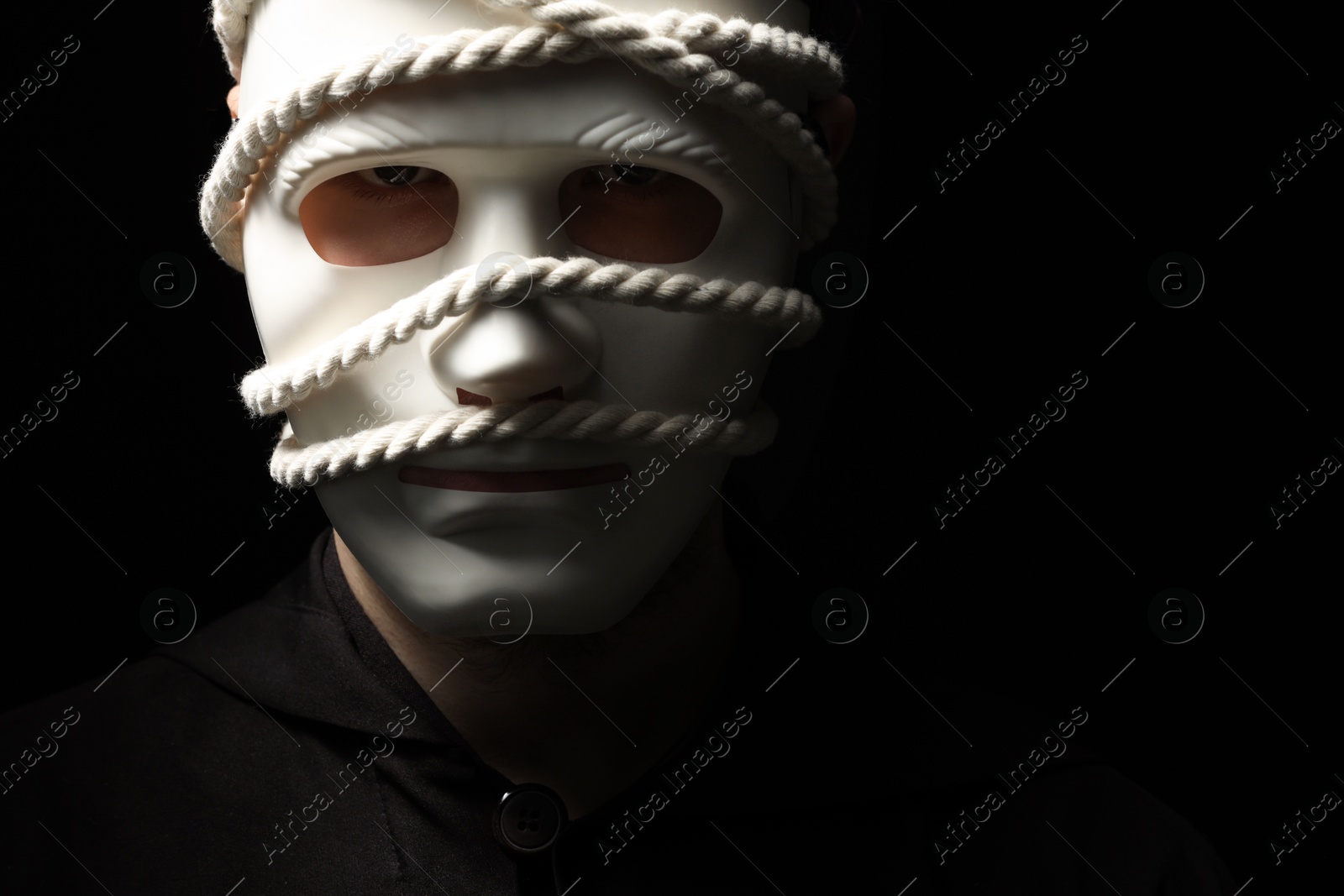 Photo of Theatrical performance. Man with plastic mask and hemp rope on black background, space for text