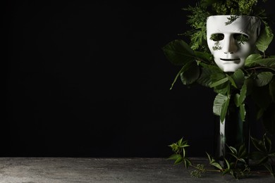 Photo of Theatrical performance. Plastic mask and floral decor on table against black background, space for text