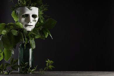 Photo of Theatrical performance. Plastic mask and floral decor on table against black background, space for text