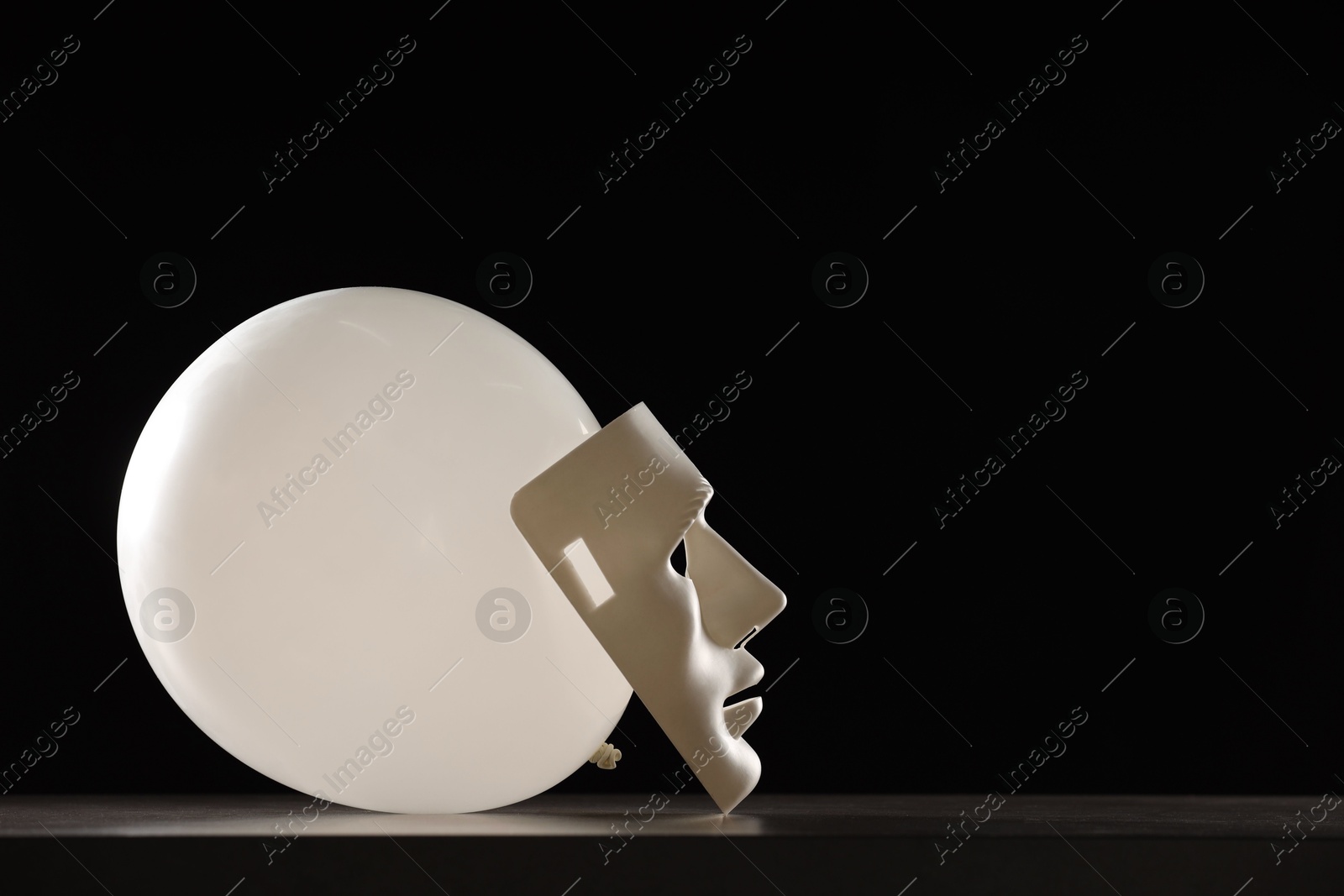 Photo of Theatrical performance. Plastic mask and white balloon on table against black background, space for text