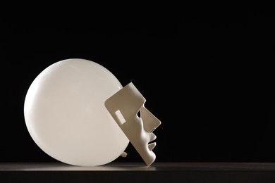 Photo of Theatrical performance. Plastic mask and white balloon on table against black background, space for text