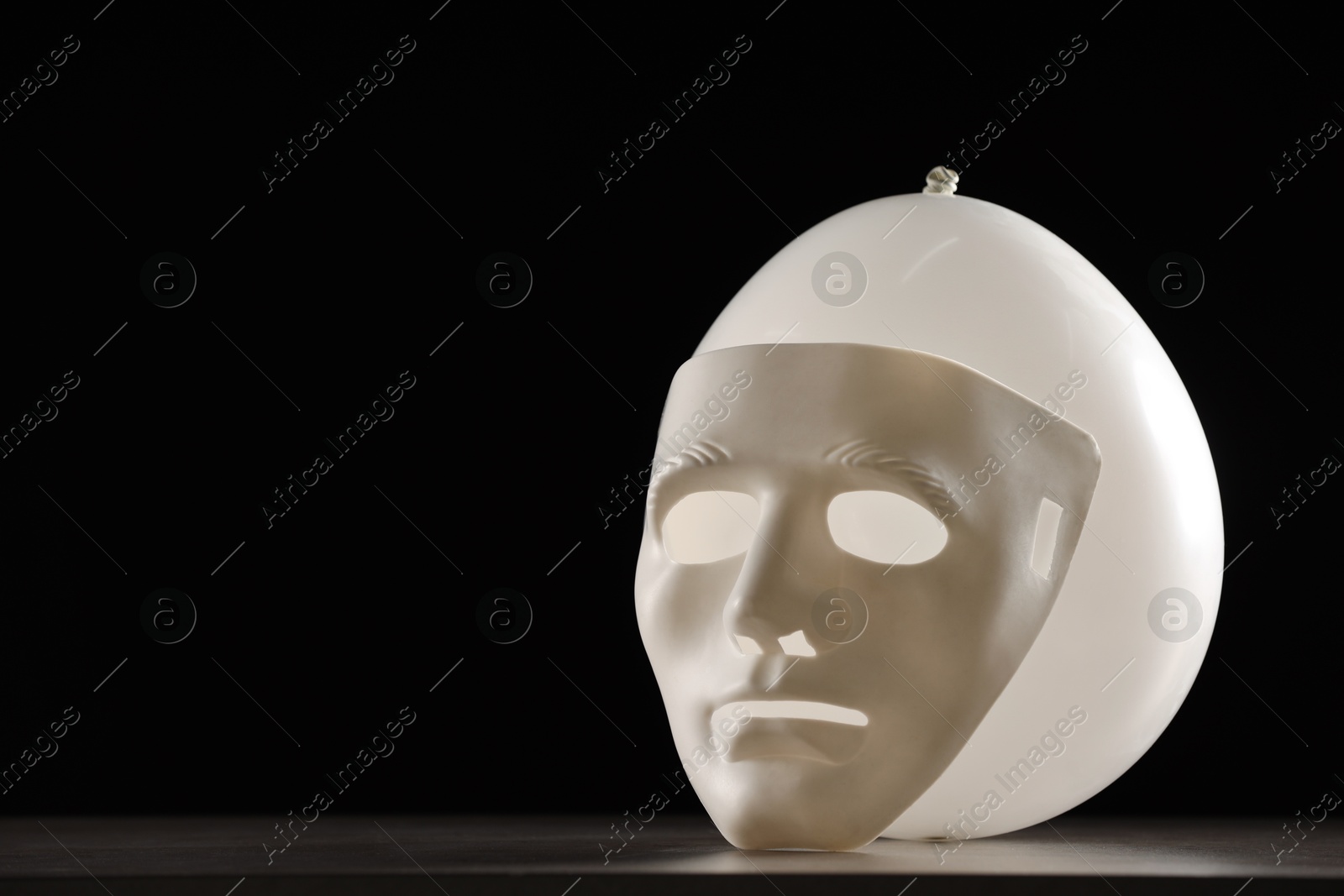 Photo of Theatrical performance. Plastic mask and white balloon on table against black background, space for text