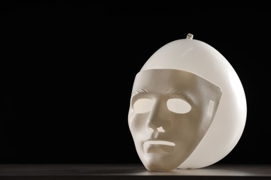 Photo of Theatrical performance. Plastic mask and white balloon on table against black background, space for text