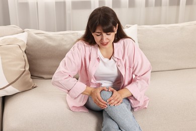 Photo of Upset woman suffering from knee pain on sofa at home