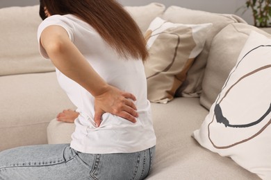 Woman suffering from back pain on sofa at home, back view