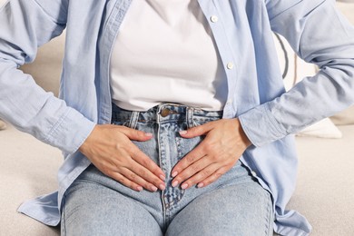 Woman suffering from abdominal pain on sofa indoors, closeup