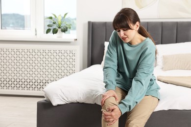 Upset woman suffering from knee pain on bed at home