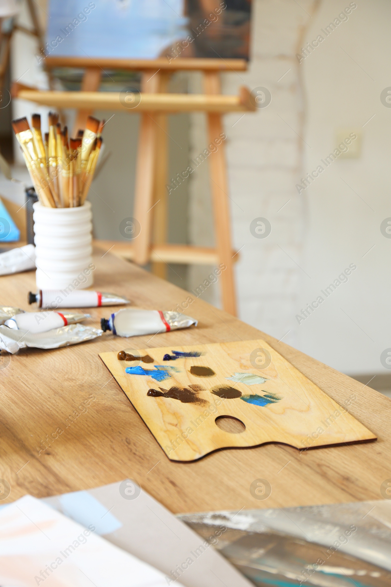 Photo of Palette, paints and brushes on wooden table in drawing studio