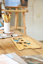 Photo of Palette, paints and brushes on wooden table in drawing studio