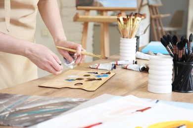 Photo of Woman with brush using palette at wooden table in drawing studio, closeup