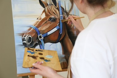 Photo of Woman drawing cute horse with brush in studio, closeup