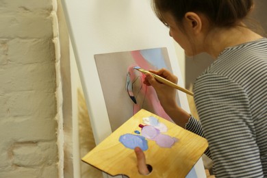 Photo of Woman drawing on easel with canvas in studio